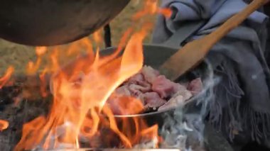 Elinde spatula olan bir adam tavada et kızartıyor ve ateş ediyor. Ağır çekimde.