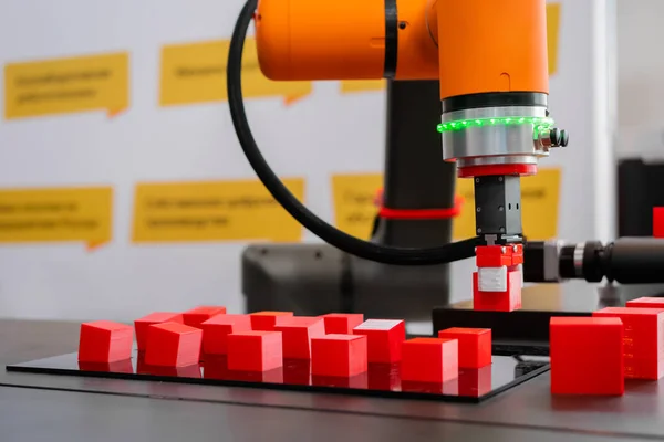 Pick and place robotic arm manipulator moving red toy blocks at robot exhibition