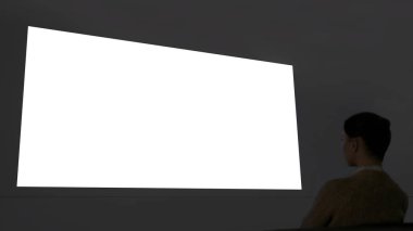Kadın büyük beyaz duvar ekranına bakıyor. Sinema taklit ediyor.