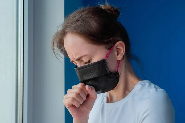 Woman with black face mask suffering from coughing, looking out of window