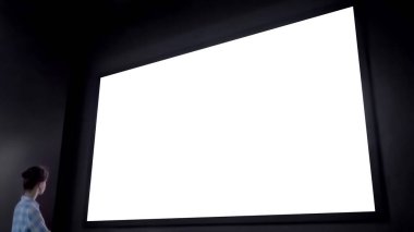 Teknoloji müzesinin karanlık odasında büyük beyaz ekrana bakan bir kadın.