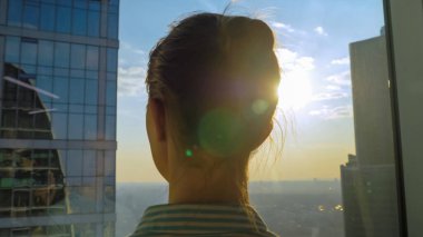 Gökdelenin cam penceresinden şehir manzarasına bakan kadının arka planı