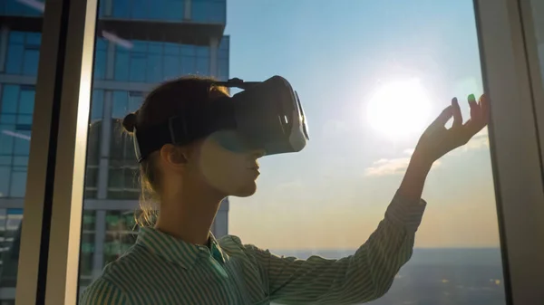 VR concept - young woman using virtual reality headset against skyscraper window