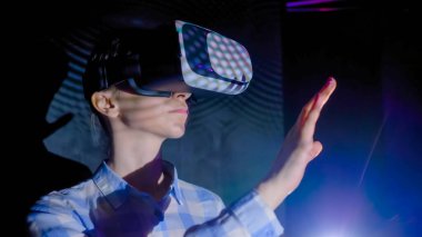 Karanlık etkileşimli VR sergisinde sanal gerçeklik kulaklığı kullanan genç bir kadın.