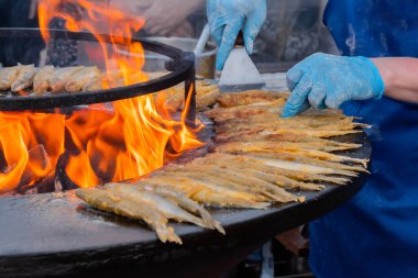 Aşçı yemek festivalinde siyah brazier üzerinde un kokulu balık pişiriyor.