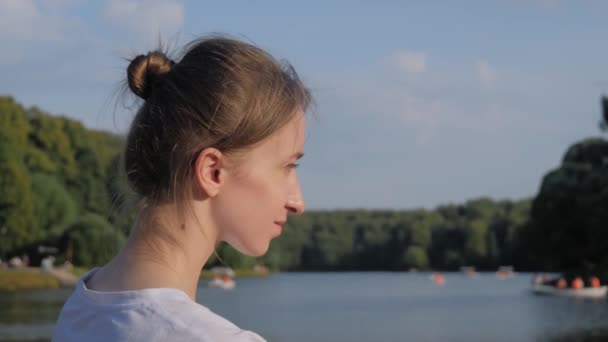 Young woman in white shirt sitting and looking at pond - slow motion — Stock Video