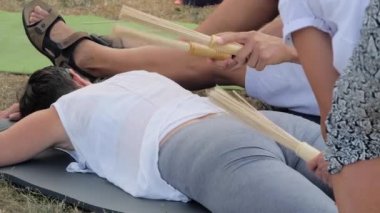 İki erkek, yoga festivalinde bambu sopalı bir kadına masaj yapıyor.