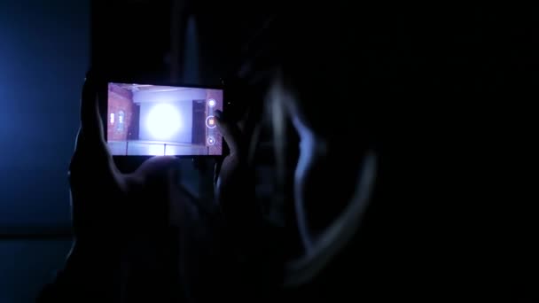 Woman holding smartphone and taking photos of video mapping show in dark room — 비디오