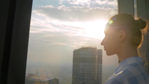 Portret van een vrouw die door het raam van de wolkenkrabber naar het stadsgezicht kijkt — Stockvideo