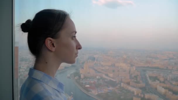 Retrato de mujer pensativa mirando paisaje urbano a través de la ventana del rascacielos — Vídeos de Stock