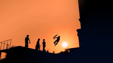 Gün batımında motosiklette yüksek atlama numaraları gösteren genç silueti - yavaş çekim