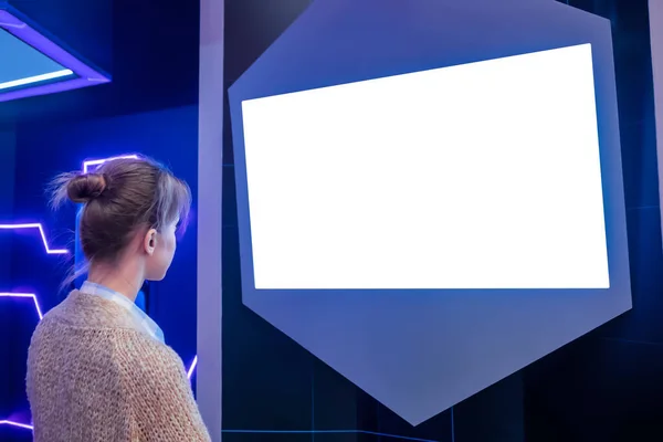 Woman looking at blank white display wall at exhibition - white screen concept