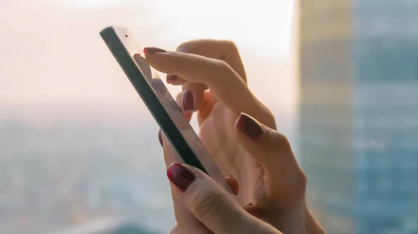 Close up side view - woman hands using smartphone device against cityscape view