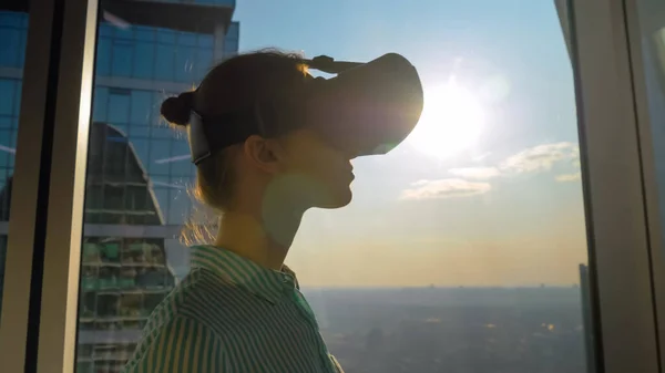 VR concept - young woman using virtual reality headset against skyscraper window