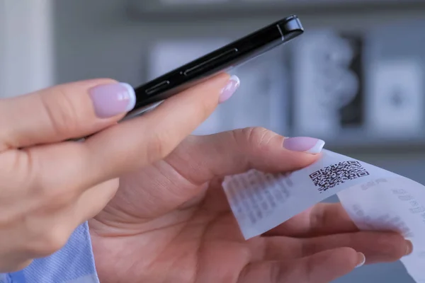Akıllı telefon kullanan ve kasiyer makbuzundaki QR kodunu tarayan bir kadın - yakın plan