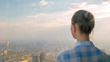 Gökdelen penceresinden şehir manzarasına bakan kadının arka planı