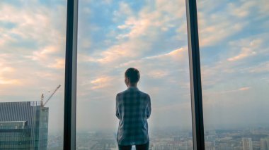 Düşünceli bir kadının gökdelen penceresinden şehir manzarasına bakışı
