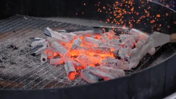 Шеф-повар держит шпатель и пытается зажечь древесный уголь со многими блестками на гриле — стоковое видео