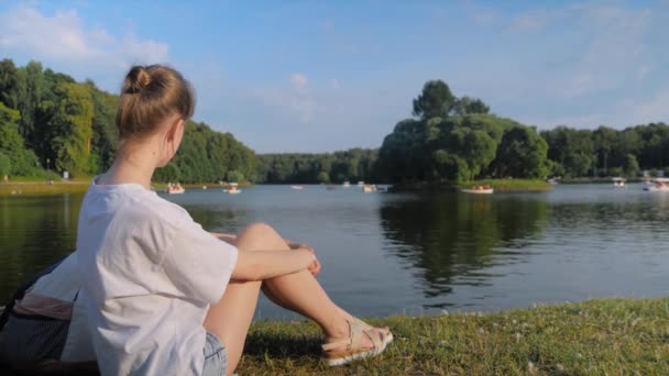 Mujer joven con camisa blanca sentada y mirando al estanque - cámara lenta — Vídeos de Stock