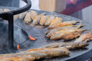 Crispy breaded european smelt fish on black brazier at outdoor food market clipart