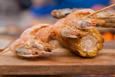 Yakın çekim: ızgara karides, karides şişi ve tahta kesme tahtasında mısır koçanı.