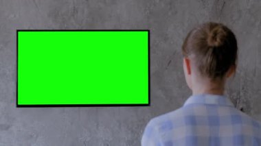 Gri oturma odasında boş yeşil ekranlı düz akıllı televizyon izleyen bir kadın.