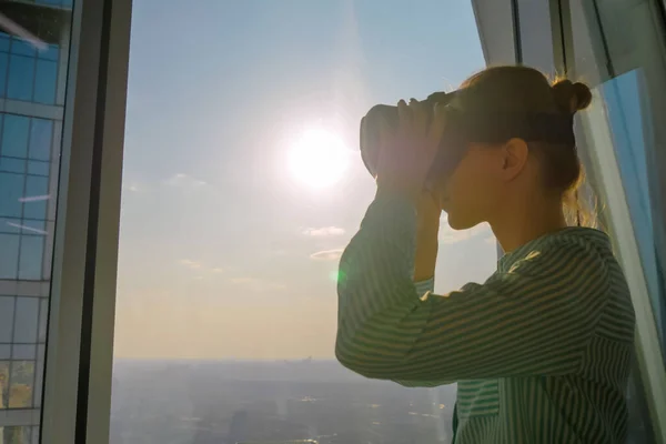 Young woman using virtual reality headset against skyscraper window - VR concept