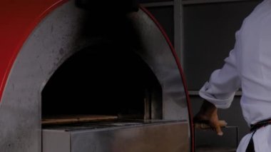 Şef, fırıncı restorandaki modern metal fırına pizza koyuyor. Kapatın.