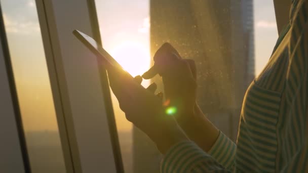 Mulher usando smartphone contra vista cityscape pôr do sol através da janela - close-up — Vídeo de Stock