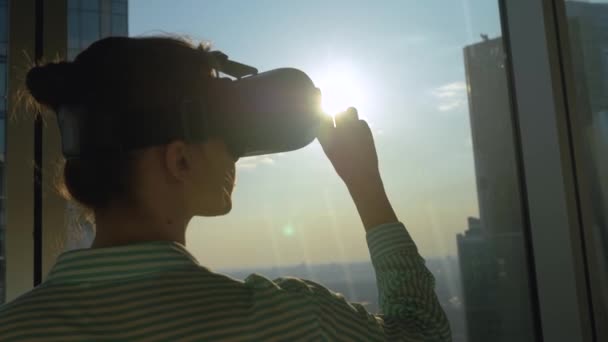 Концепція VR - молода жінка використовує гарнітуру віртуальної реальності проти вікна хмарочоса — стокове відео