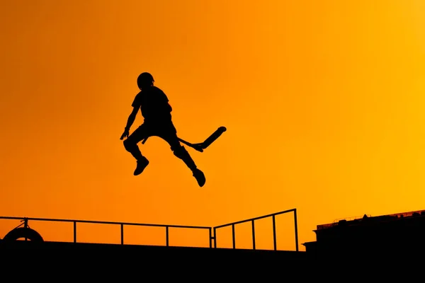 Teenager silhouette showing high jump tricks on scooter against sunset sky