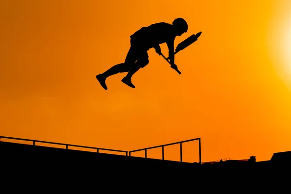 Teenager silhouette showing high jump tricks on scooter against sunset sky