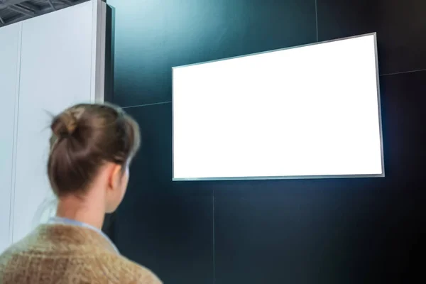 Woman looking at blank white display wall at exhibition - white screen concept