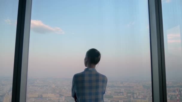 Пенсионерка смотрит на город из окна небоскреба - вид сзади — стоковое видео
