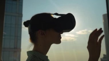Ağır çekim: kadın VR kulaklık kullanıyor, elini gökdelen penceresine doğru hareket ettiriyor