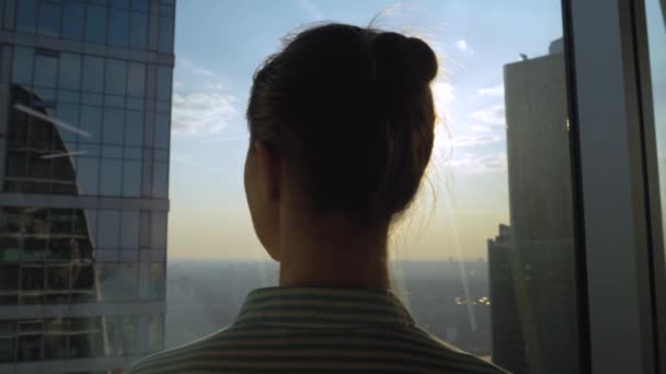Mujer pensativa mirando paisaje urbano a través de la ventana del rascacielos - vista trasera — Vídeos de Stock