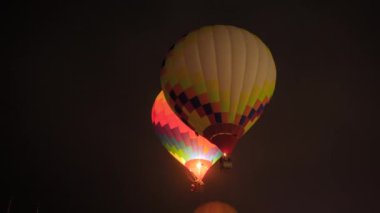 İki renkli sıcak hava balonu karanlık gökyüzüne karşı alevlerle uçuyor.