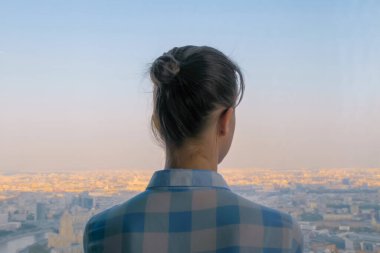 Düşünceli bir kadının gökdelen penceresinden şehir manzarasına bakışı