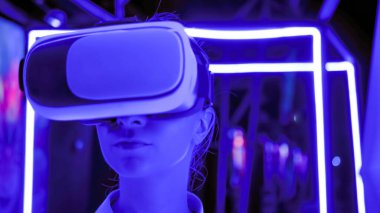 Karanlık etkileşimli VR sergisinde sanal gerçeklik kulaklığı kullanan genç bir kadın.
