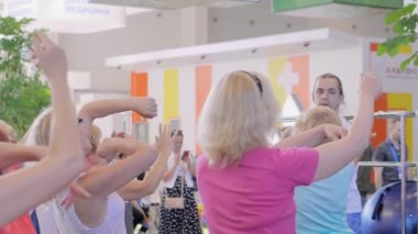 Bir grup yaşlı insan spor sergisinde birlikte qigong egzersizi yapıyor.