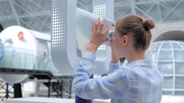 Young woman looking through white telescope and exploring exhibition — Stock Video