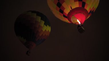 İki renkli sıcak hava balonu karanlık gökyüzüne karşı alevlerle uçuyor.