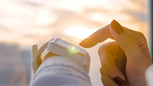 Woman using wearable white smartwatch against warm sunset sky - close up