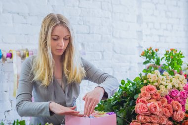 Çiçekçide çiçeklerle hediye kutusu yapan profesyonel bir çiçekçi.