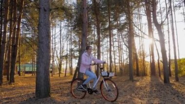 Sonbahar parkında gün batımında bisiklete binen genç bir kadın. Ağır çekim.
