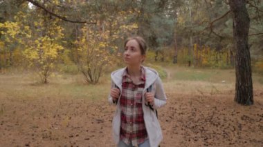 Sırt çantalı genç bir kadının sonbahar parkında yürüyüşünün ön görüntüsü.