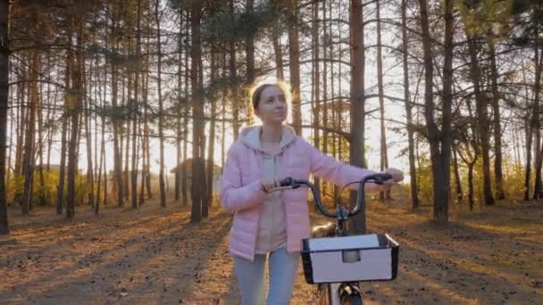 Slow motion: ung kvinna går med cykel i höstens stadspark - utsikt framåt — Stockvideo