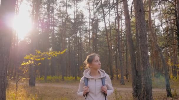 Sırt çantalı bir kadın sonbahar parkında yürüyor. Sabit çekim, güneş mercekleri parlıyor. — Stok video
