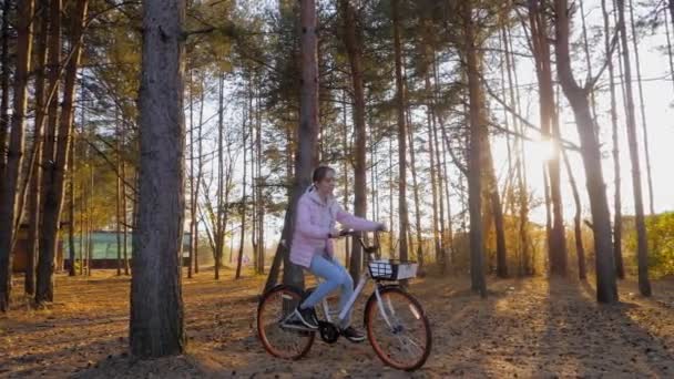 Sonbahar parkında gün batımında bisiklete binen genç bir kadın. Ağır çekim. — Stok video