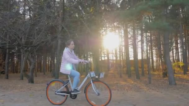 Jovem mulher andando de bicicleta no outono parque da cidade ao pôr-do-sol - câmera lenta — Vídeo de Stock